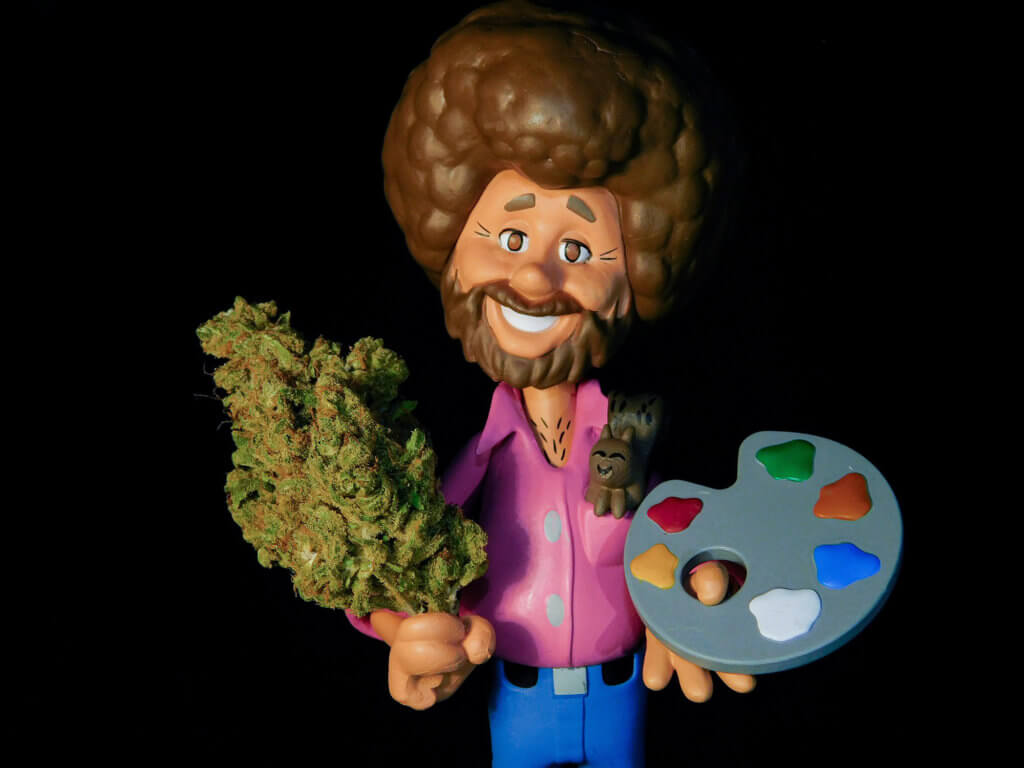 Toy figurine of Bob Ross holding a cannabis bud instead of a paint brush